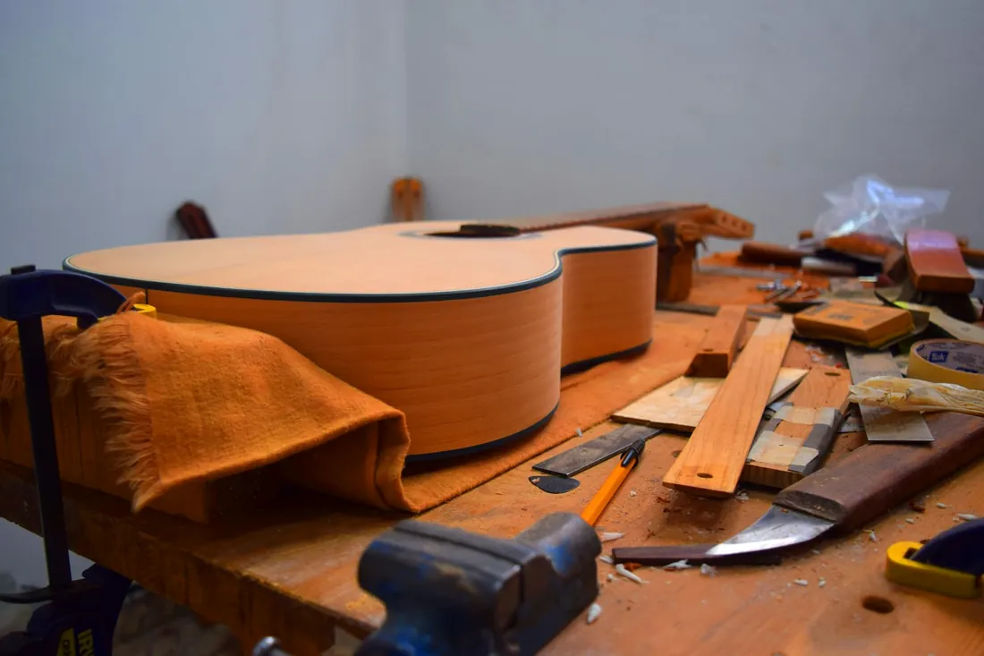 Guitarra acústica sin barnizar apoyada en el banco de un taller, rodeada de gubias, listones y virutas de madera